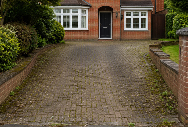 Driveway entrance in Bedford before cleaning with weeds, moss and dull paving near the front of the home