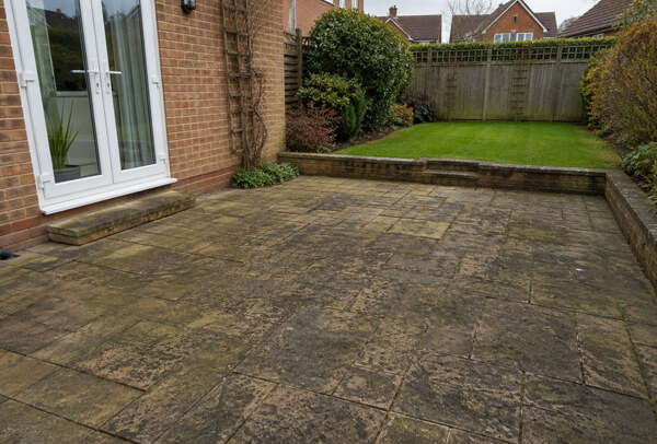 Patio in Bedford before cleaning, with algae, grime and darker marks across the paving